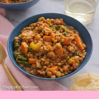 Pinterest graphic of a bowl of lentil soup by a glass of wine and a spoon.