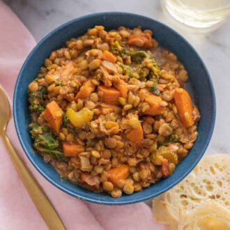 Overhead view of a bowl of lentil soup by a linen napkin, spoon, and bread.