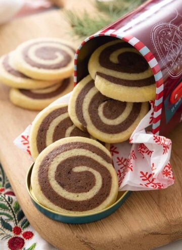 A Christmas tin with pinwheel cookies coming out of it.