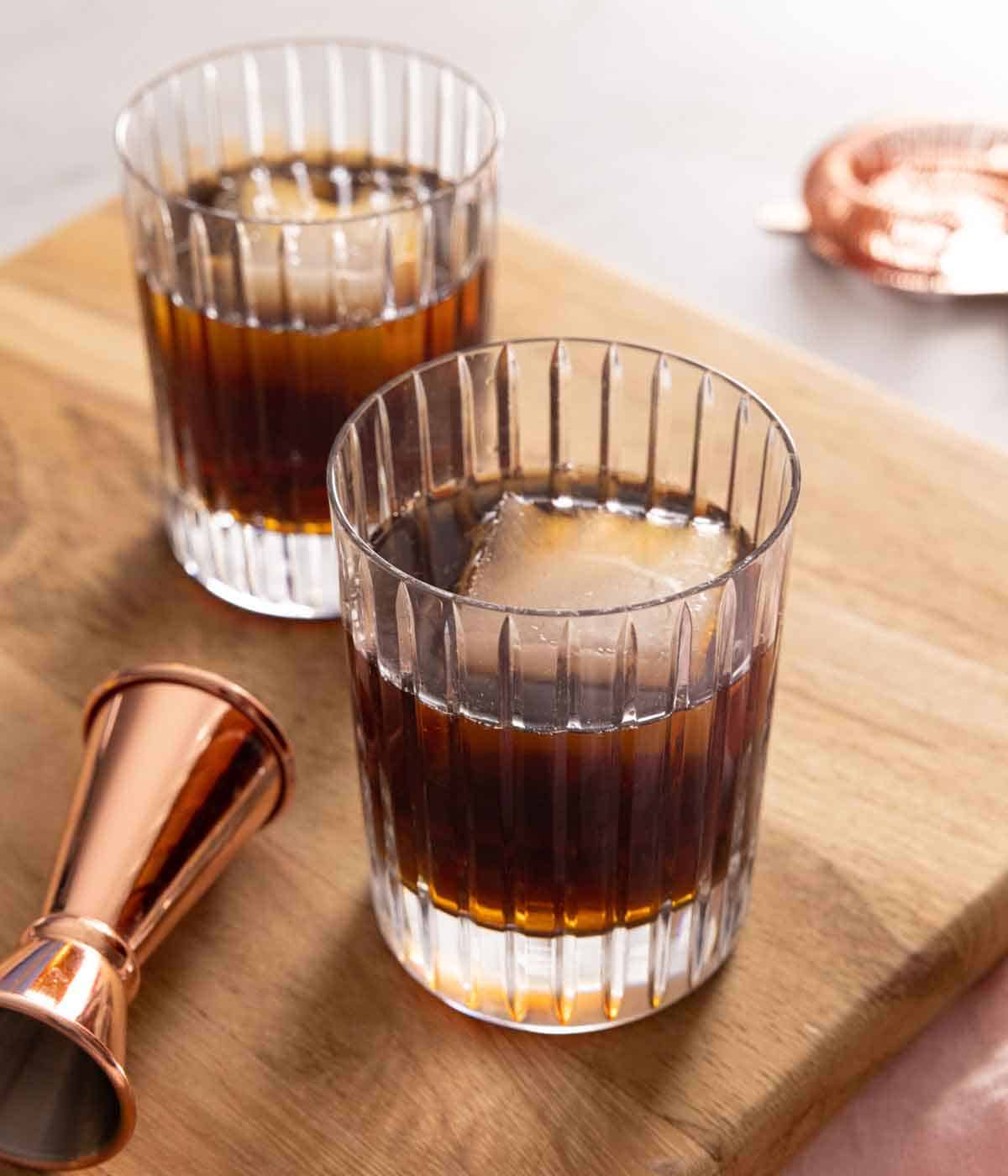 Two glasses of Black Russian cocktails with a jigger beside it.