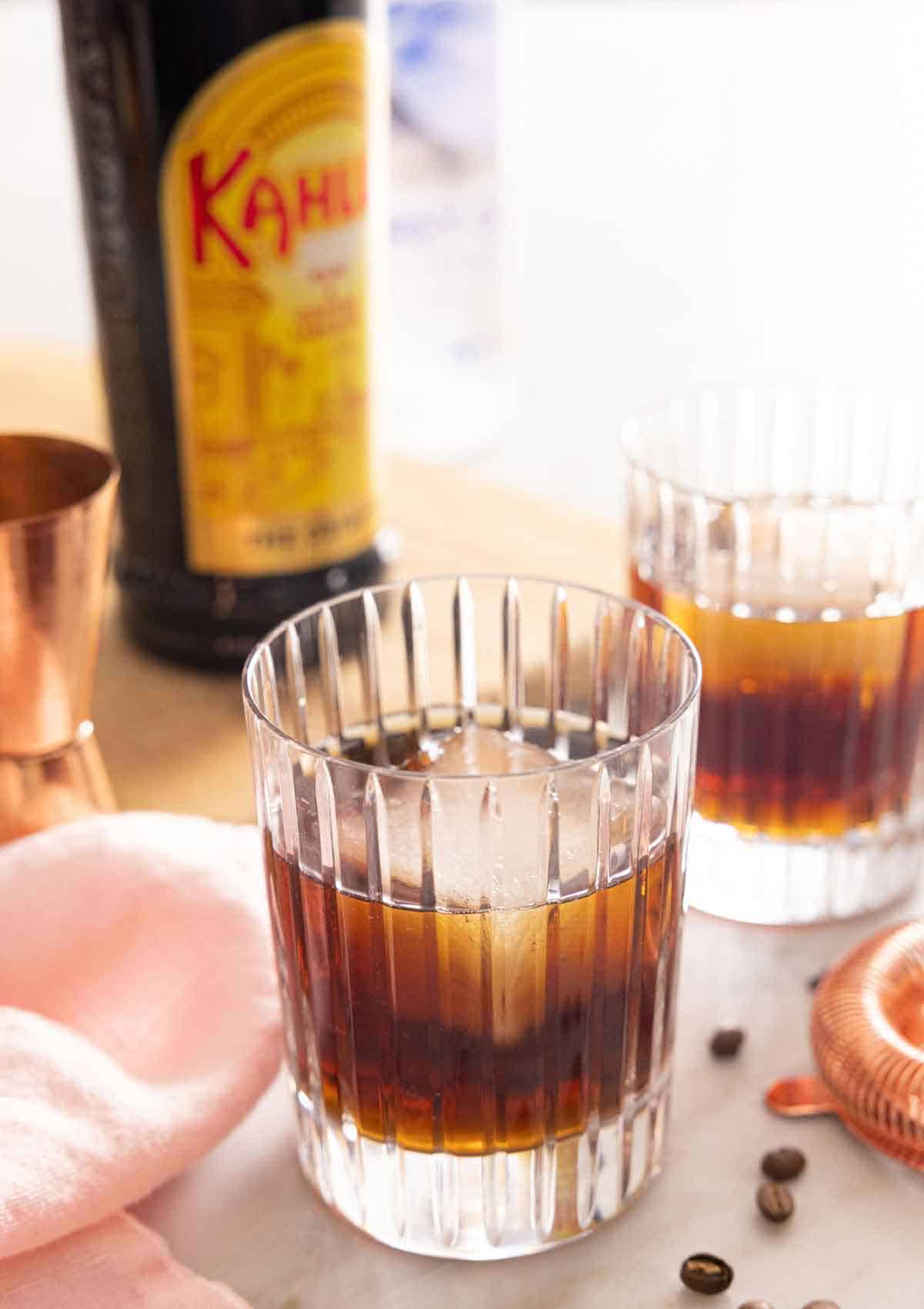 Two glasses of Black Russians with one in front. A bottle of Kahlua in the background.