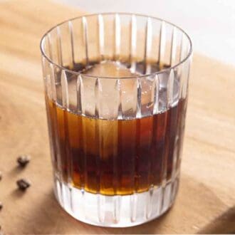 A glass of Black Russian on a wooden board with coffee beans.