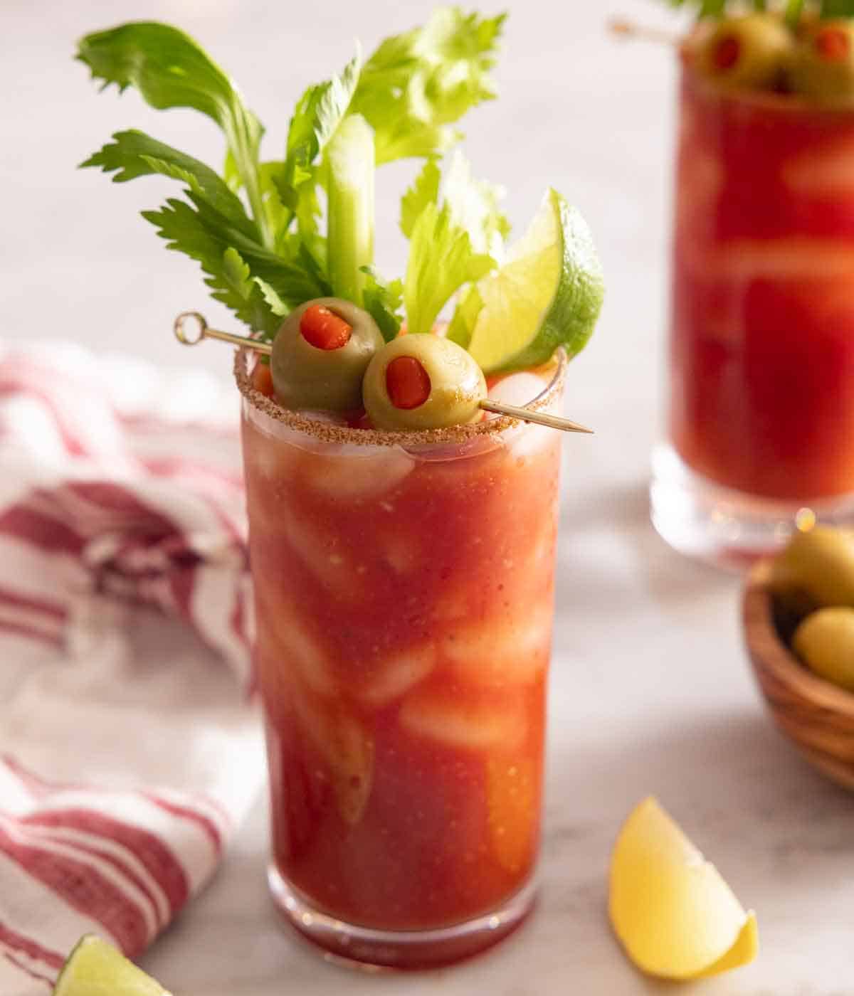 A glass of Bloody Mary with two olives, lime wedge, and celery as garnish.