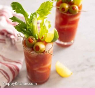 Pinterest graphic of two glasses of Bloody Mary with olives, limes, and celery garnishes.