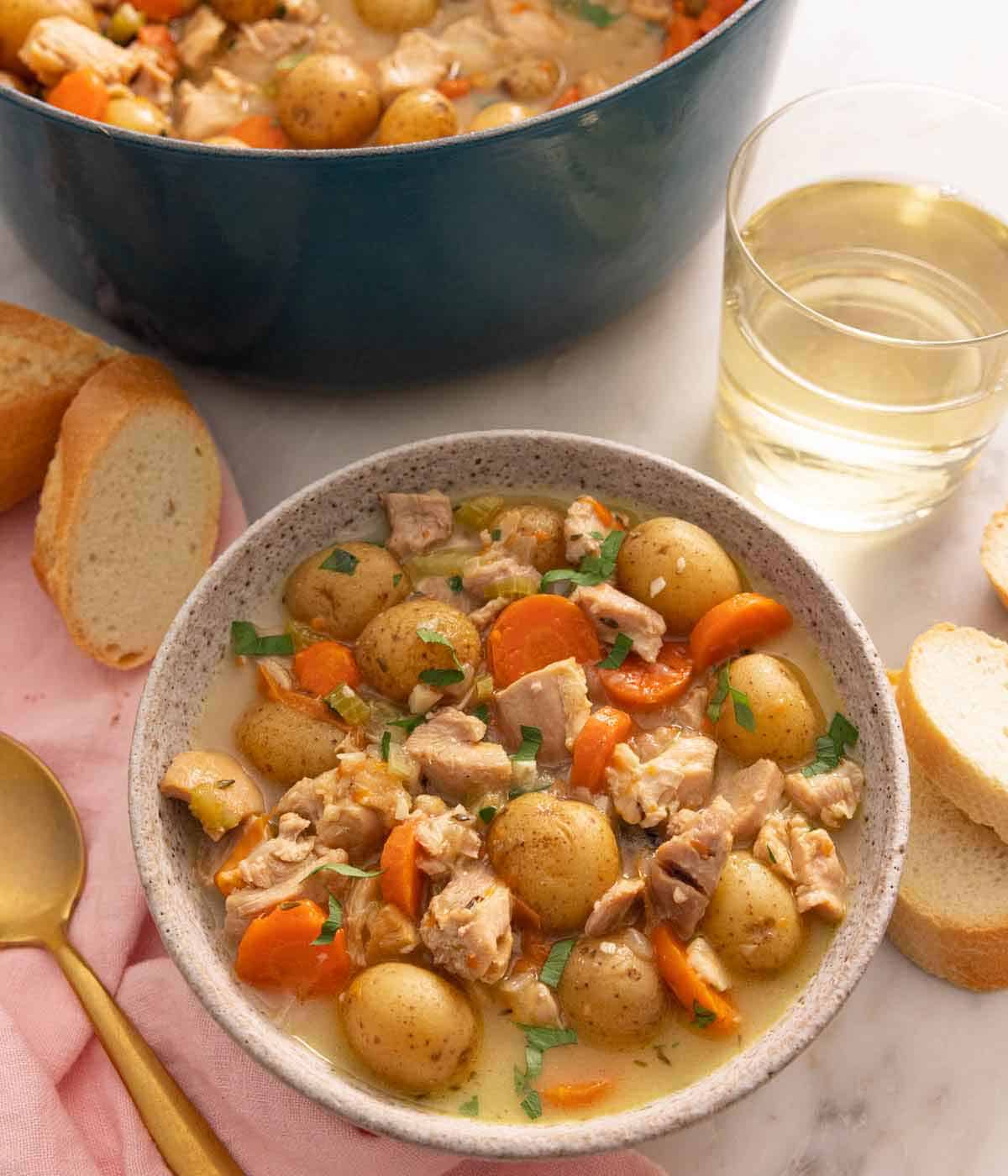 Overhead view of a bowl of chicken stew by a pot and glass of wine.
