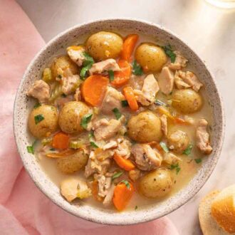 Overhead view of a bowl of chicken stew with sliced bread beside it.