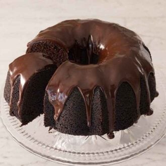 A chocolate bundt cake on a cake stand with one slice cut and slightly pulled out.