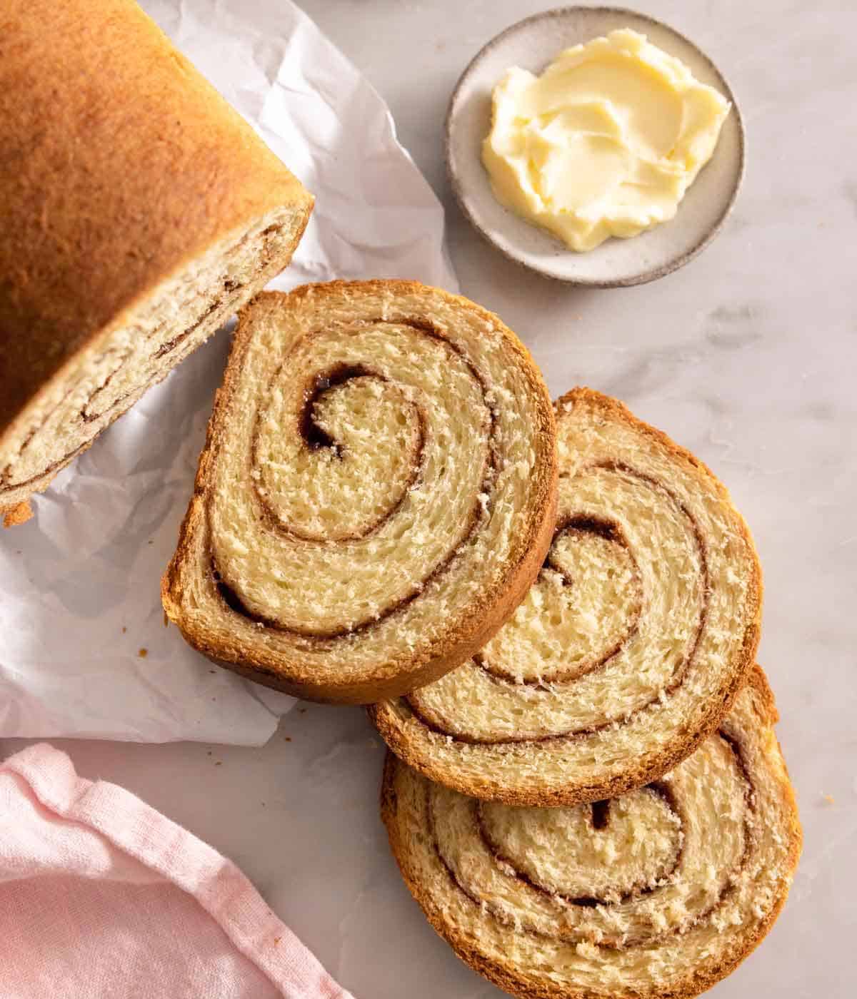 Overhead view of three slices of cinnamon swirl bread by a plate of butter.