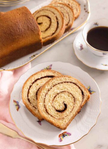 Two slices of cinnamon swirl bread on a plate by a mug of coffee.