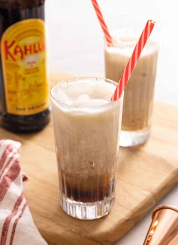 Two glasses of Colorado Bulldog cocktails with a straw with Kahlua in the background.