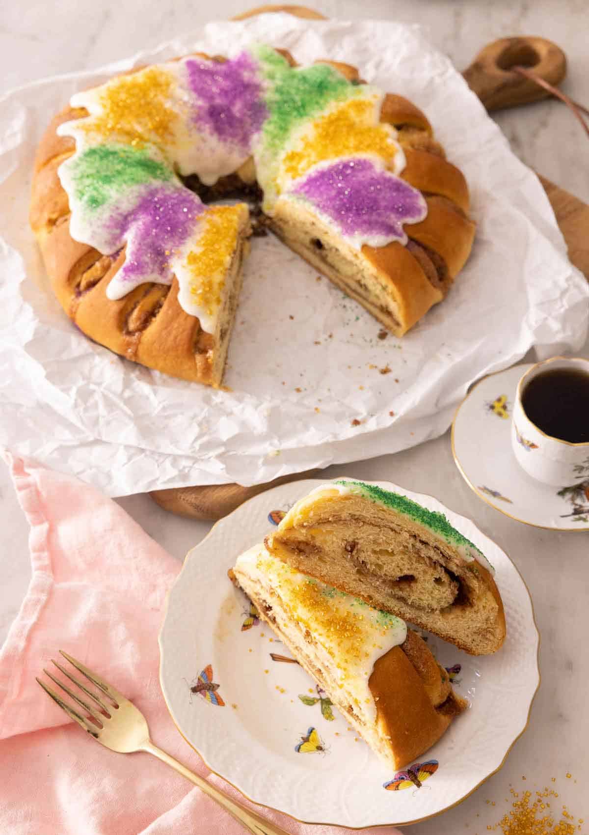 A king cake with two slices cut out, set on a plate in front of it.