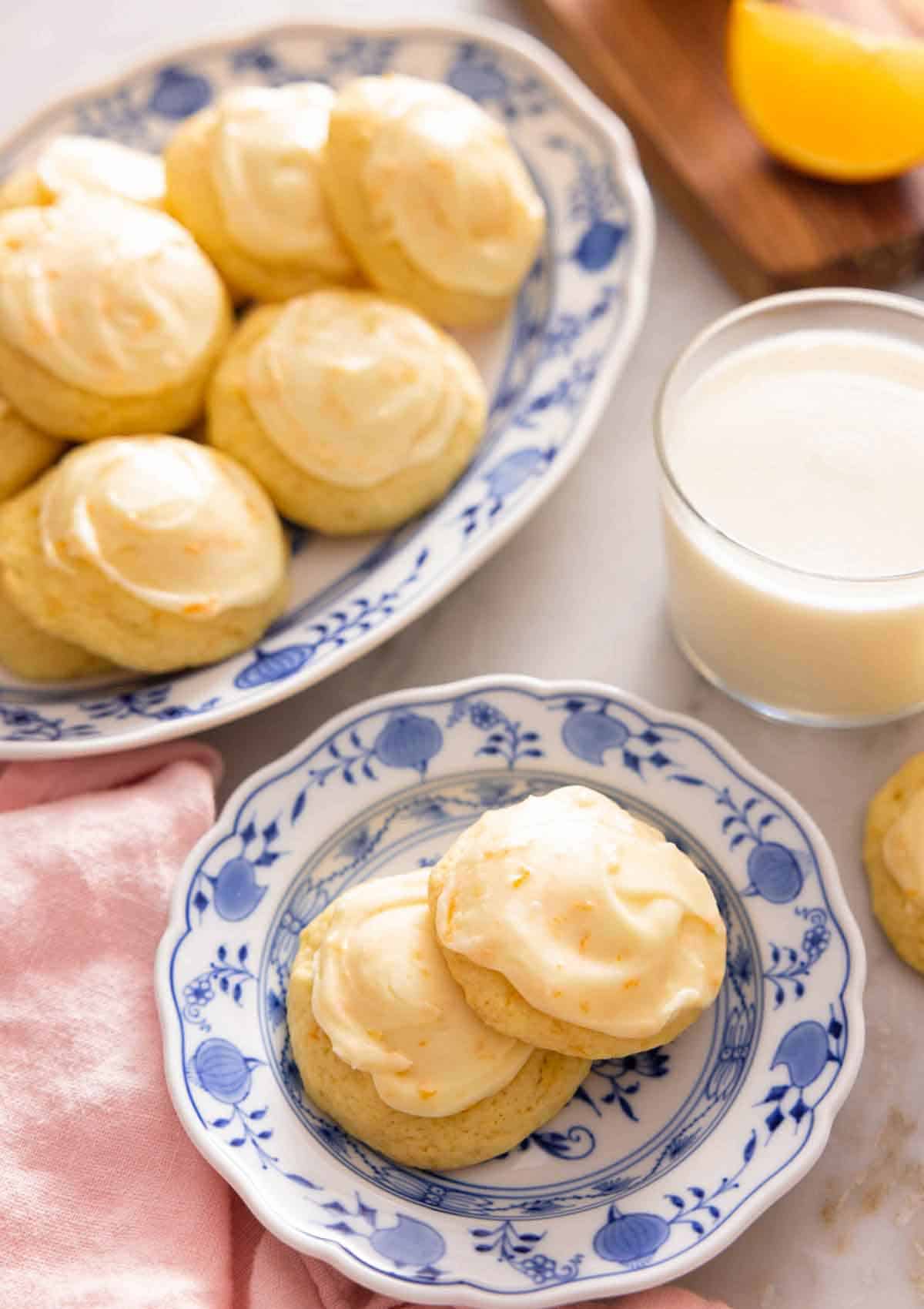 A plate with two orange cookies in front of a platter of them.