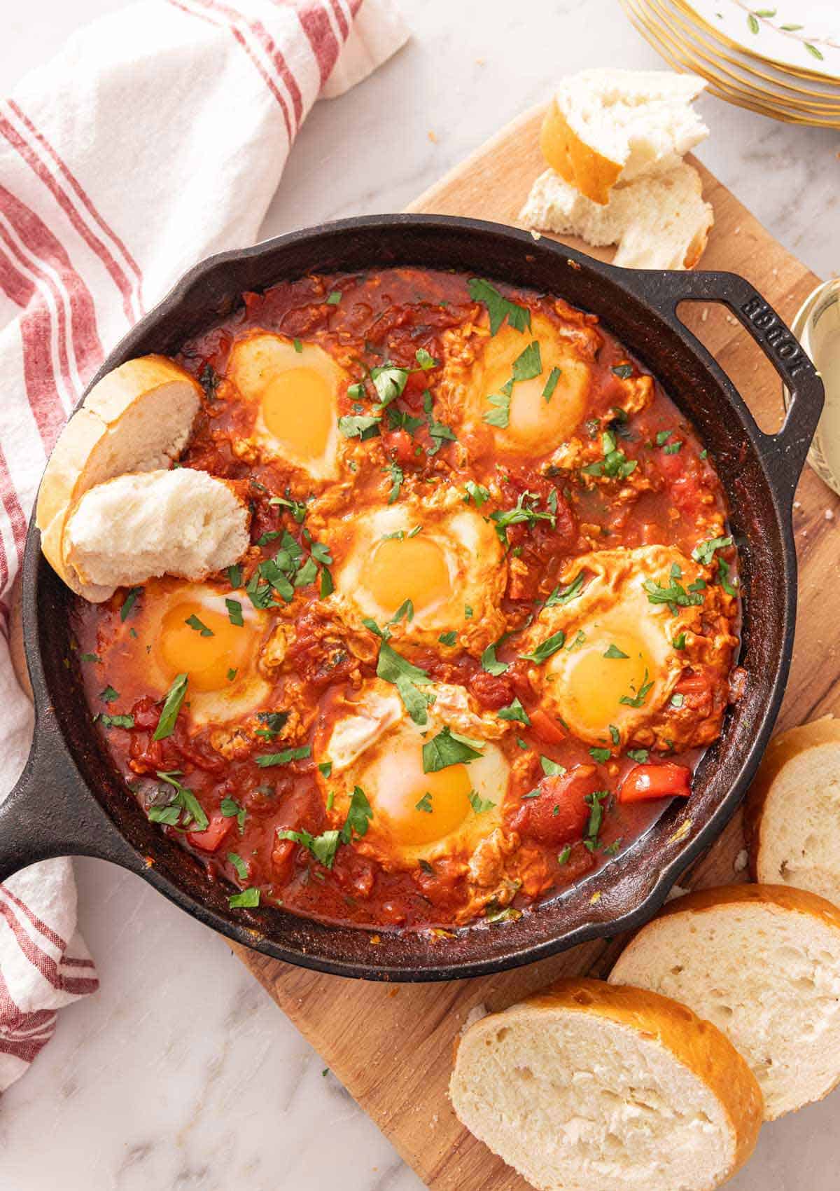 Overhead view of a cast-iron of shakshuka with bread dipped in and around the pan.