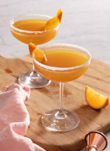 Two cocktail glasses with sidecar with an orange garnish.