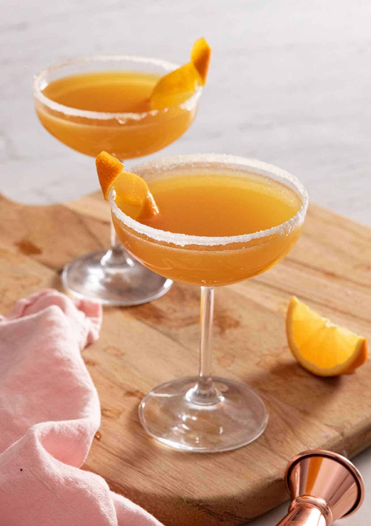 Two cocktail glasses with sidecar with an orange garnish.
