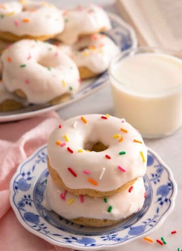 A plate with two stacked baked donuts with glaze and sprinkles on top.