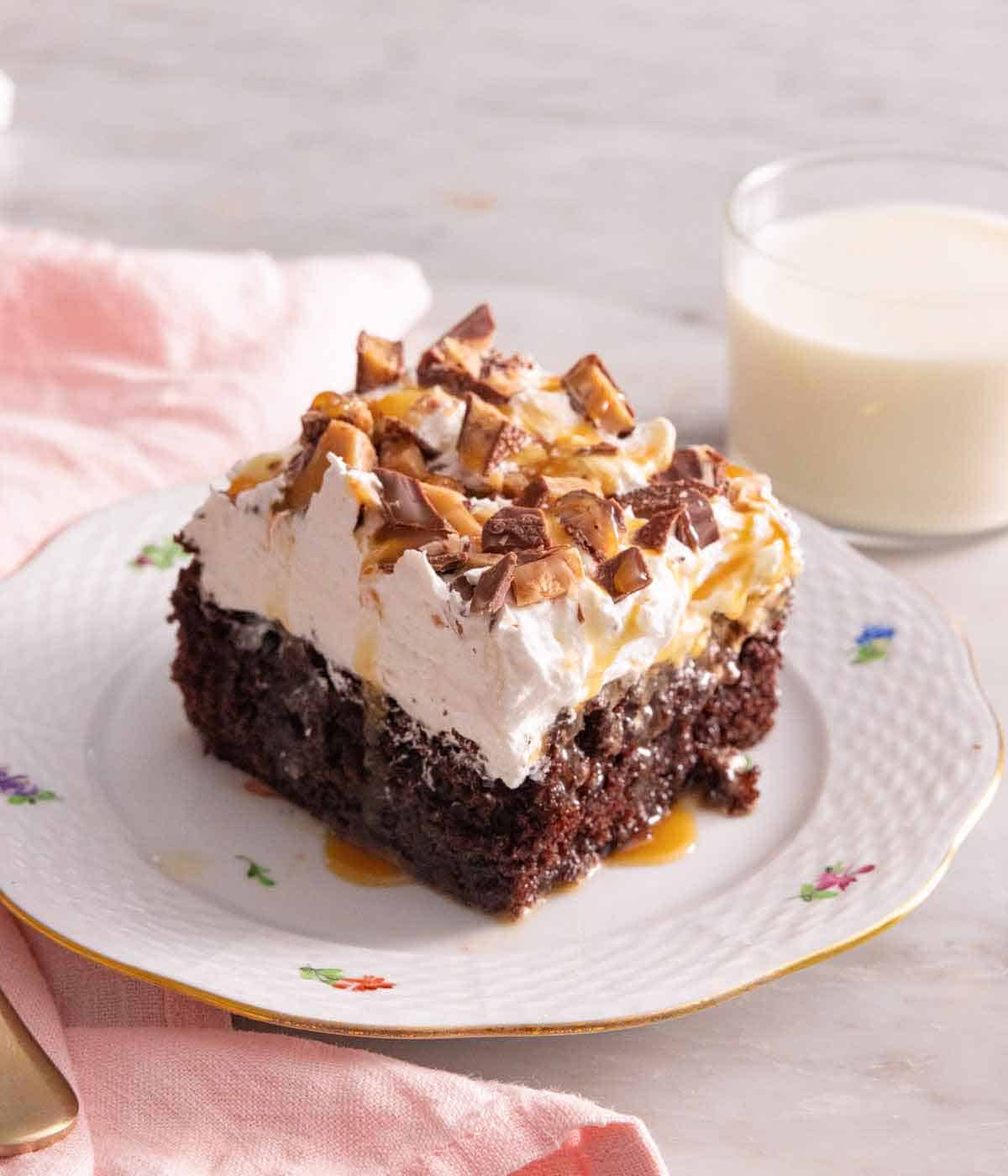 A plate with a slice of better than sex cake with a cup of milk behind it.