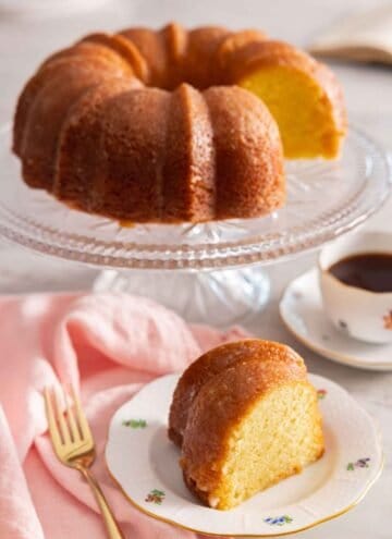 A slice of butter cake on a plate in front of the rest of the cake.