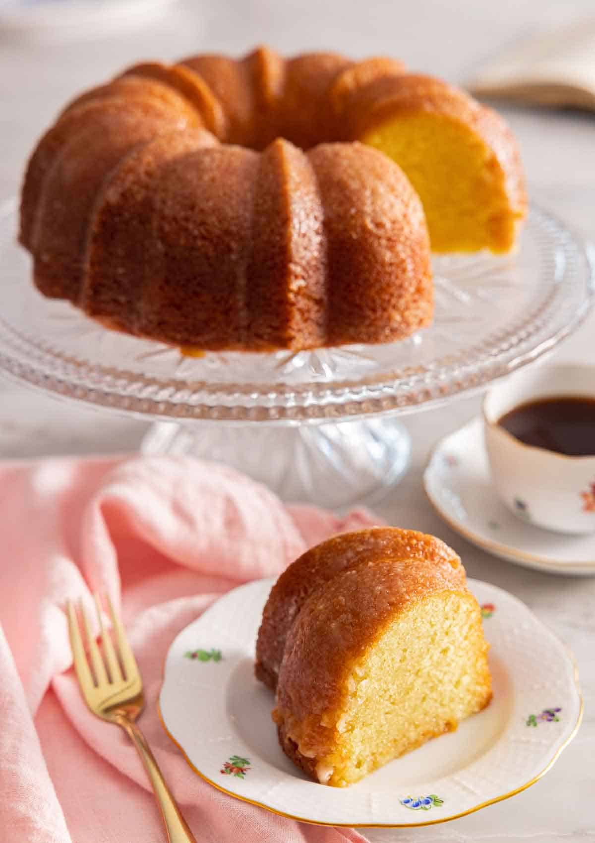 A slice of butter cake on a plate in front of the rest of the cake.