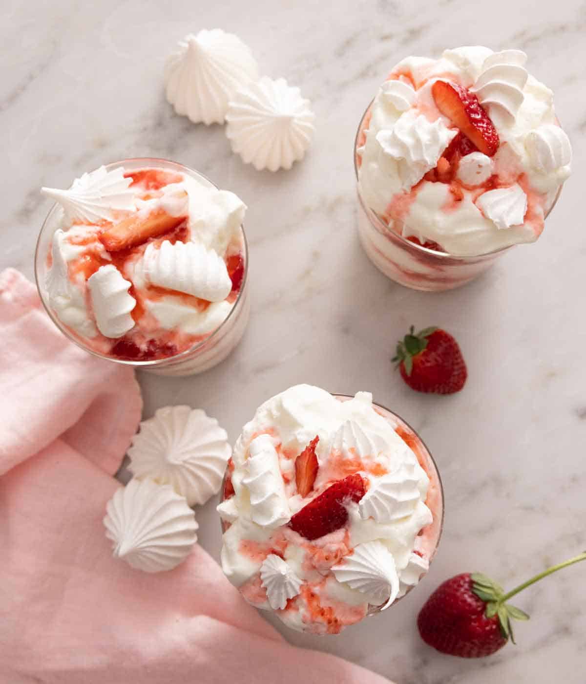 Overhead view of three Eton mess with strawberries and meringue cookies scattered around.