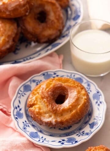 A plate with an old fashioned donut in front of a glass of milk.