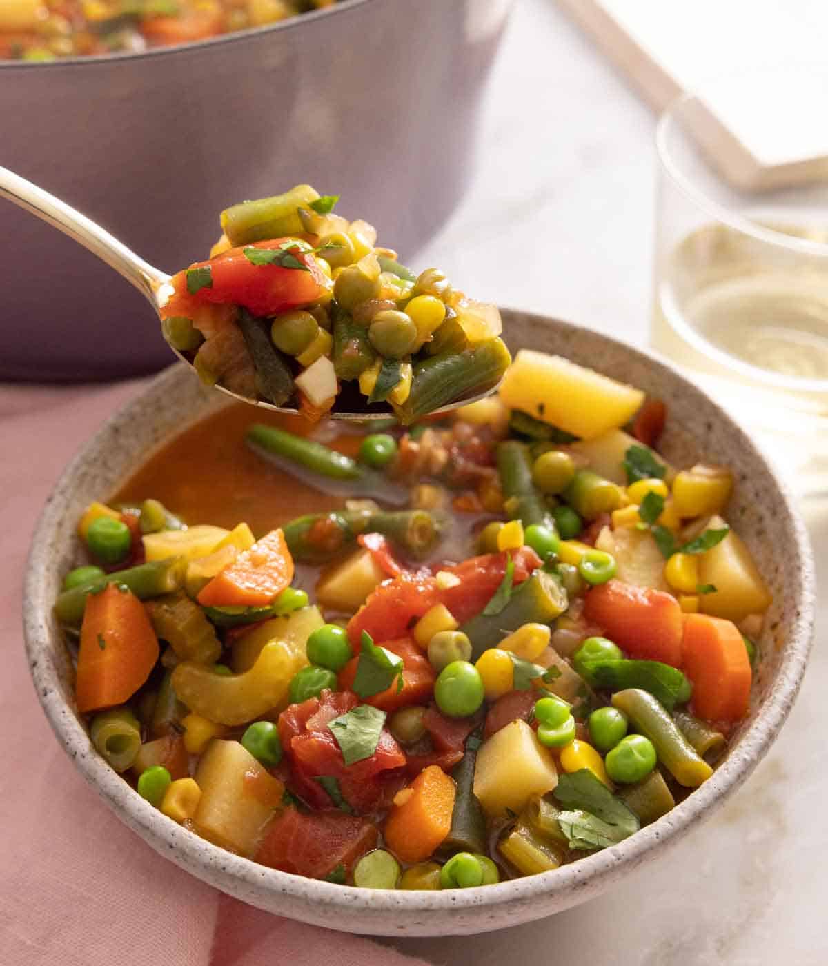 A spoonful of vegetable soup lifted from a bowl.