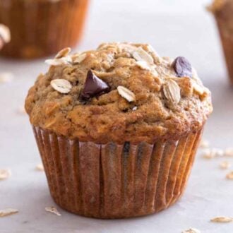 A banana oatmeal muffin in focus with oats scattered around and more muffins in the background.
