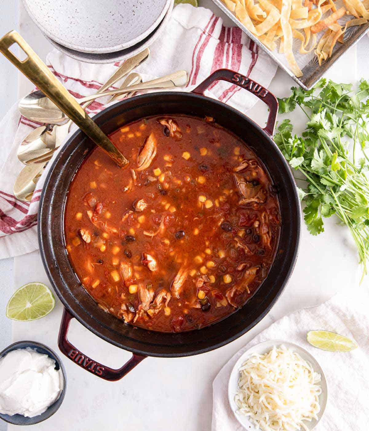 Overhead view of a dutch oven with chicken tortilla soup. Toppings scattered around.