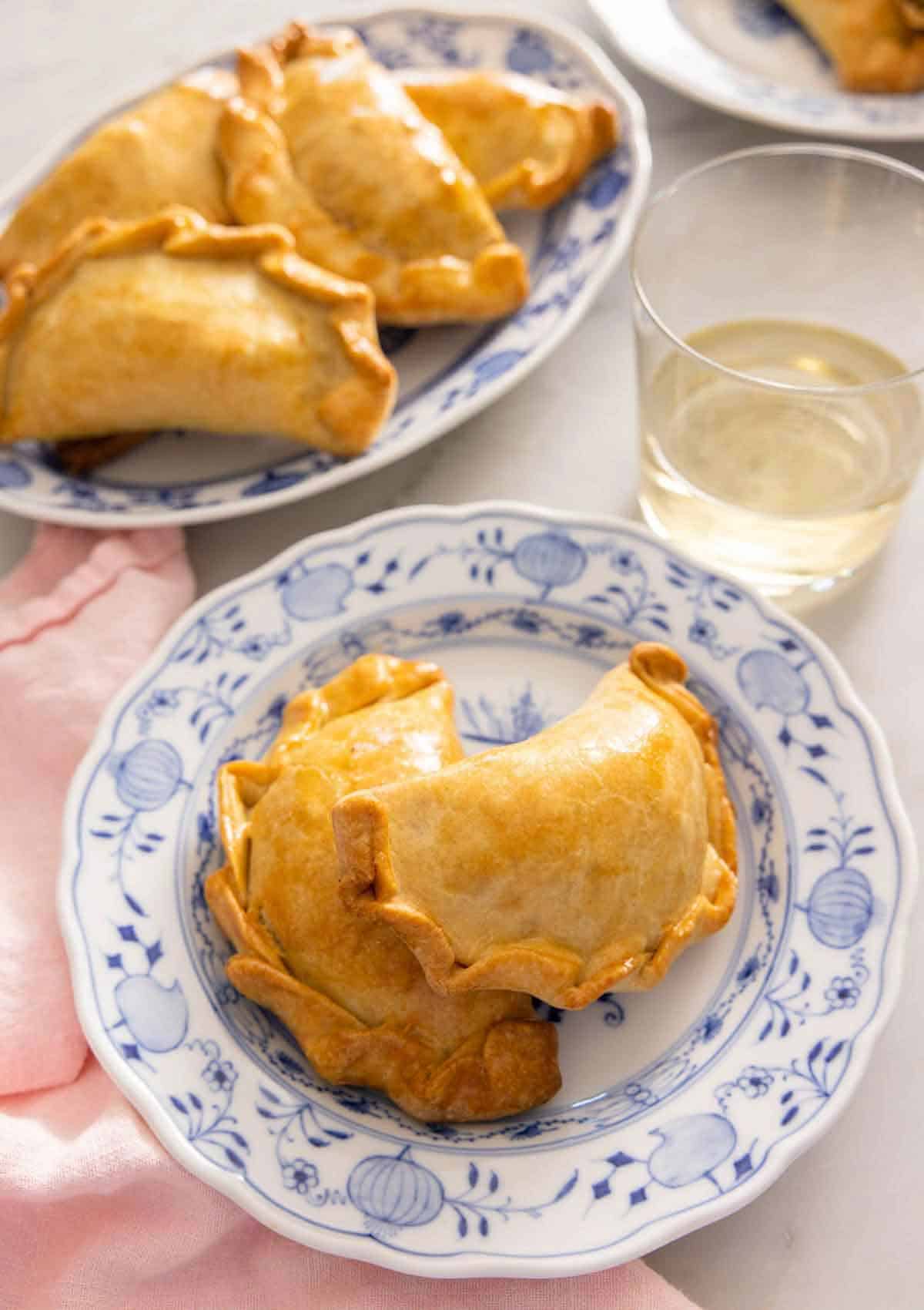 A plate with two empanadas by a plate with more.