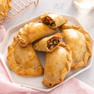A platter with five empanadas, one cut opened.