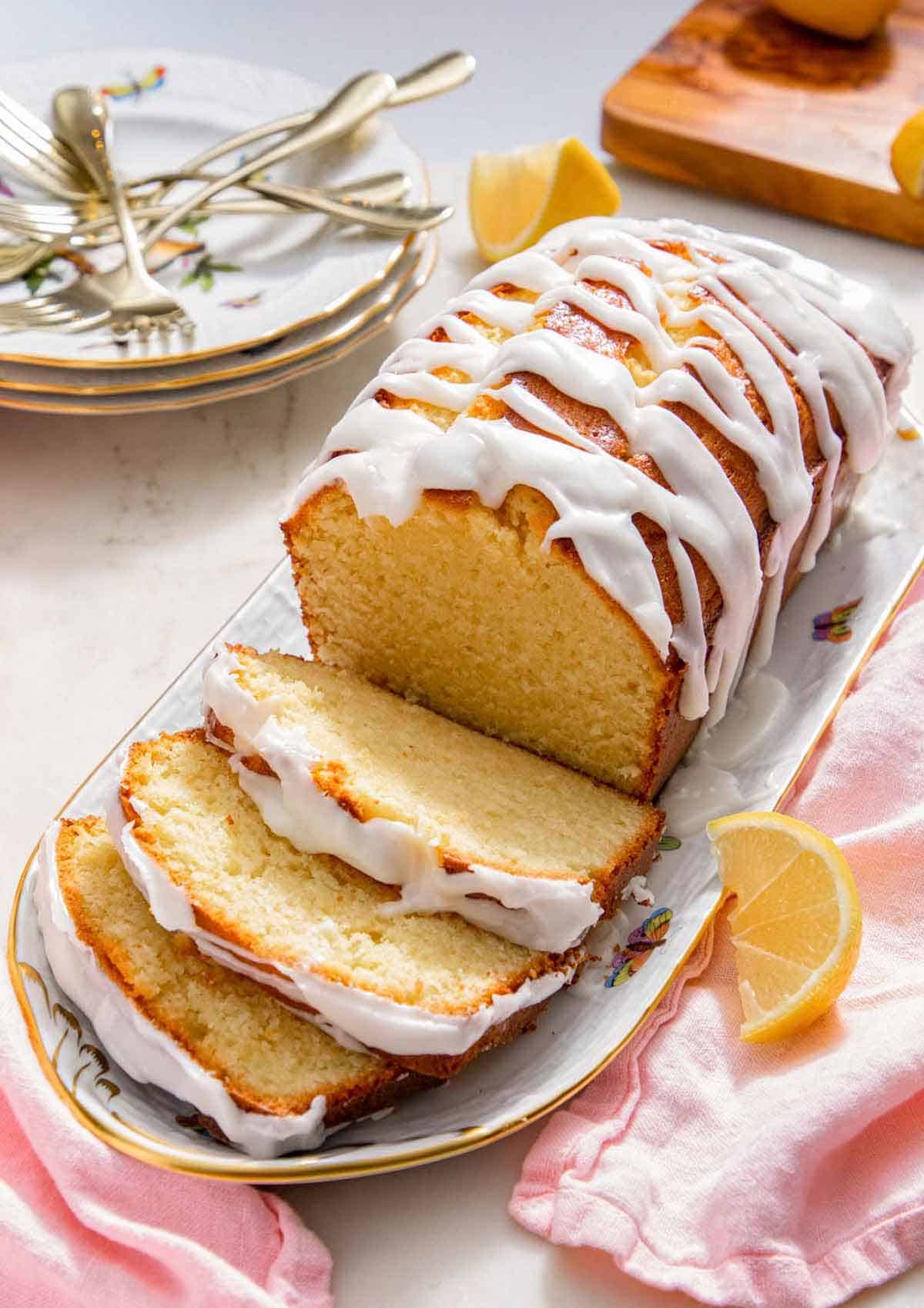 A platter with a loaf of lemon pound cake with three slices cut.