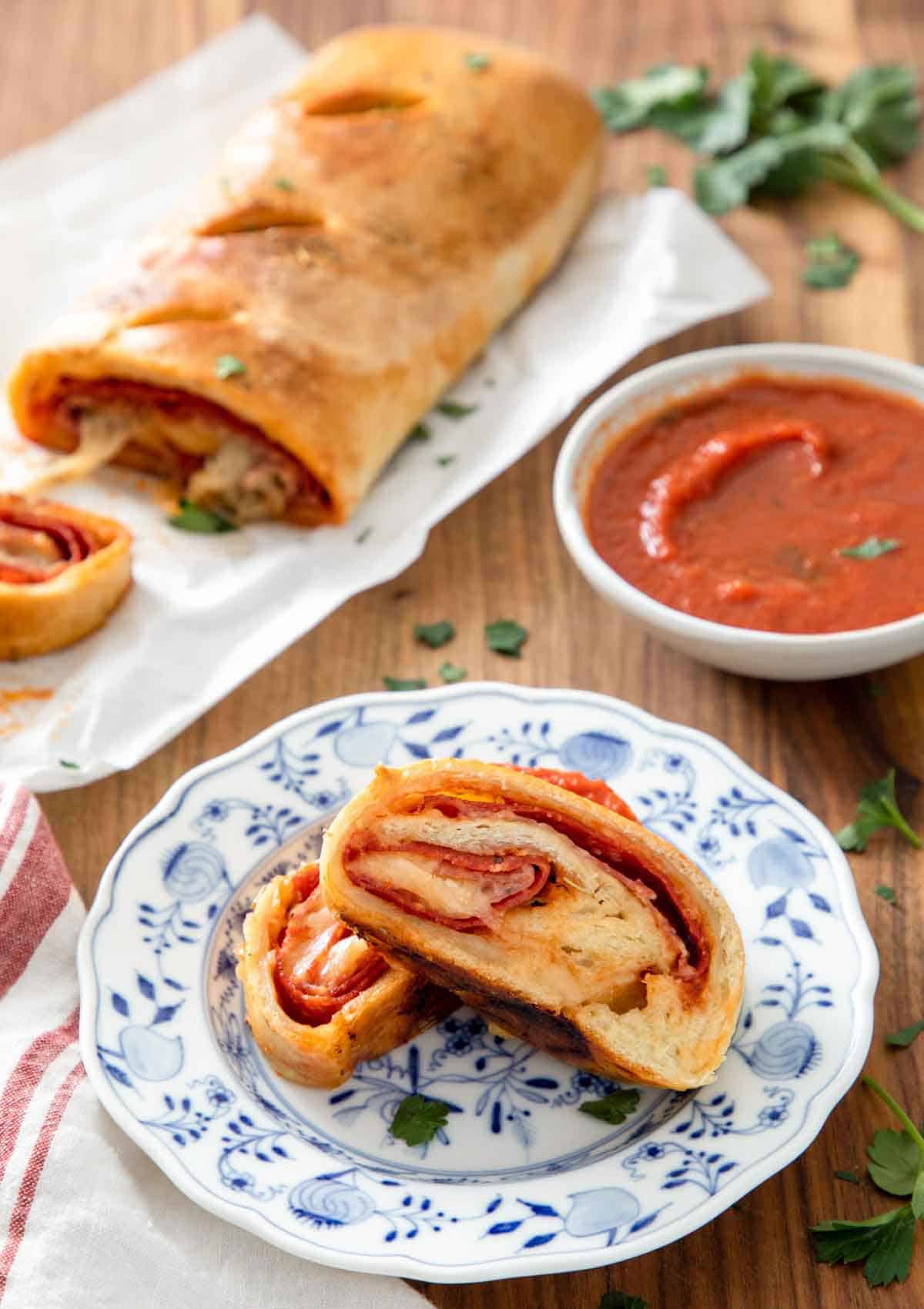 Two pieces of stromboli on a plate by some sauce and the rest of the stromboli.