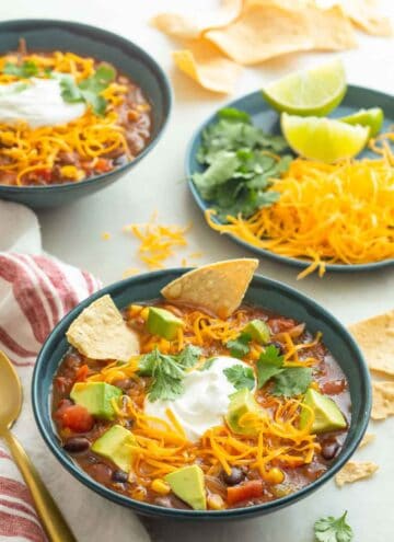 Two bowls of taco soup with a plate of toppings on the side.