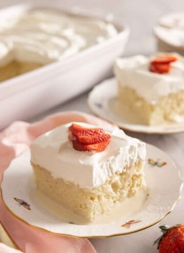 Two plates, one in front, with a square slice of tres leches cake.