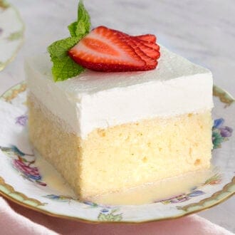 A square slice of tres leches cake with strawberry on top.