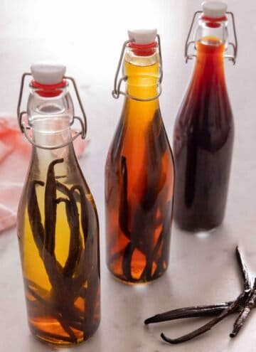 Three bottles of homemade vanilla extract with three vanilla beans beside it.