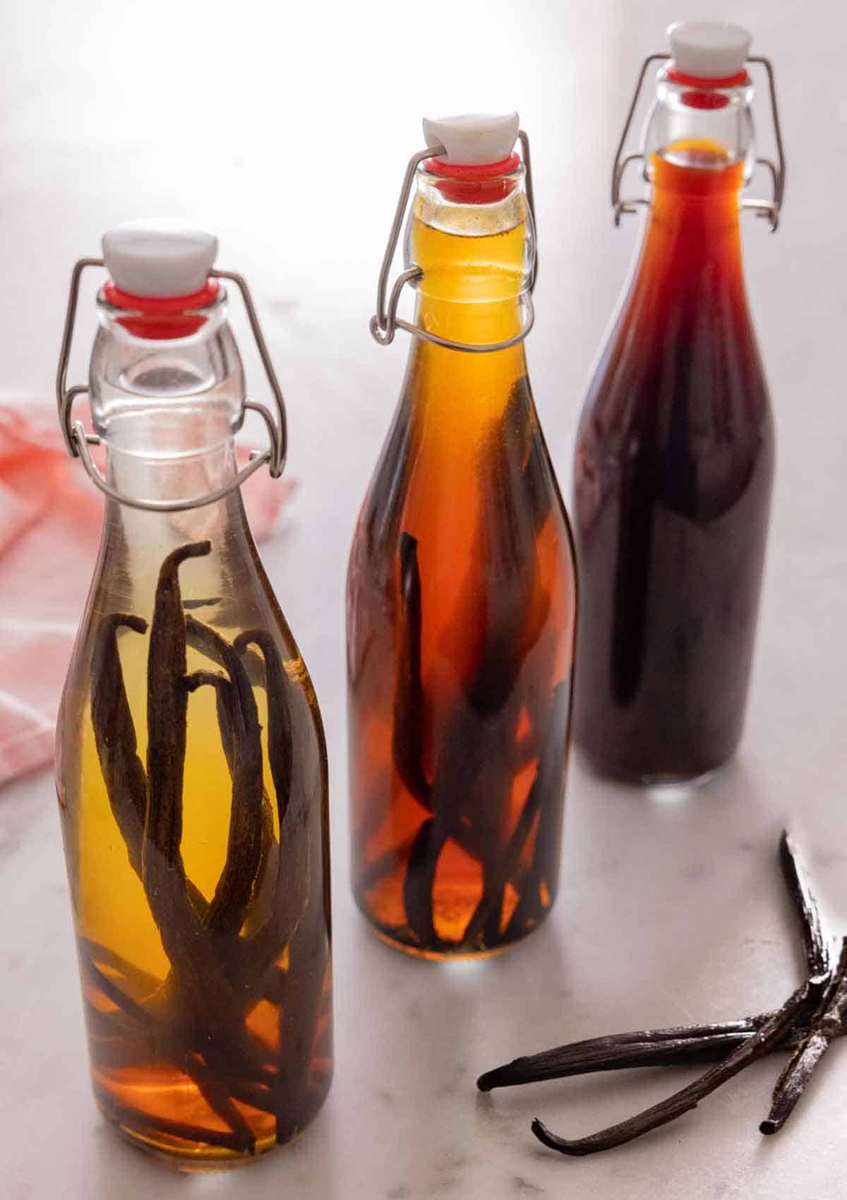 Three bottles of homemade vanilla extract with three vanilla beans beside it.