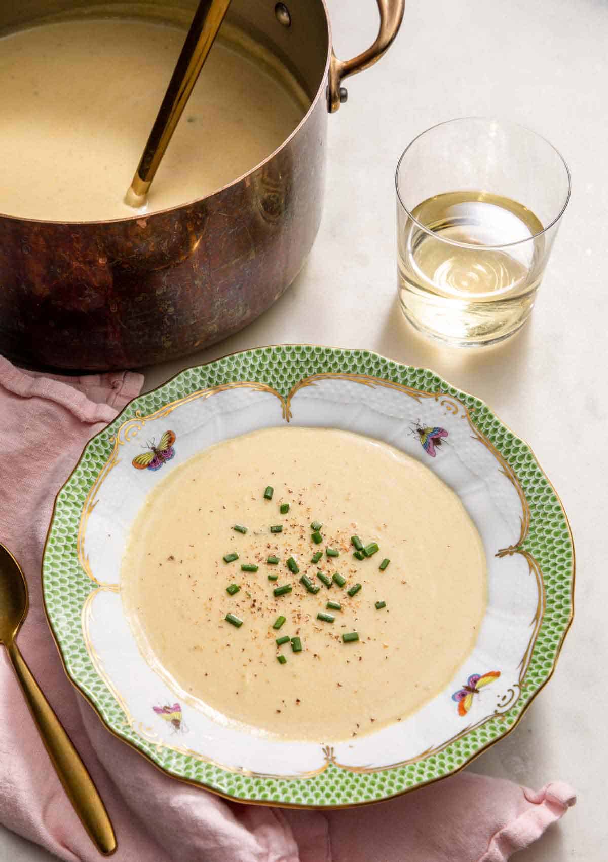 A bowl of vichyssoise with chives on top by a glass of wine and more soup.