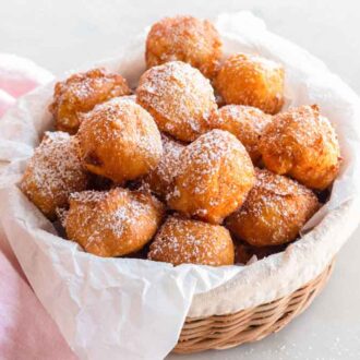 A basket of zeppole with a pink linen beside it.