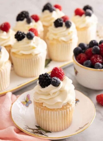 An angel food cupcake on a plate in front of a platter of cupcakes.