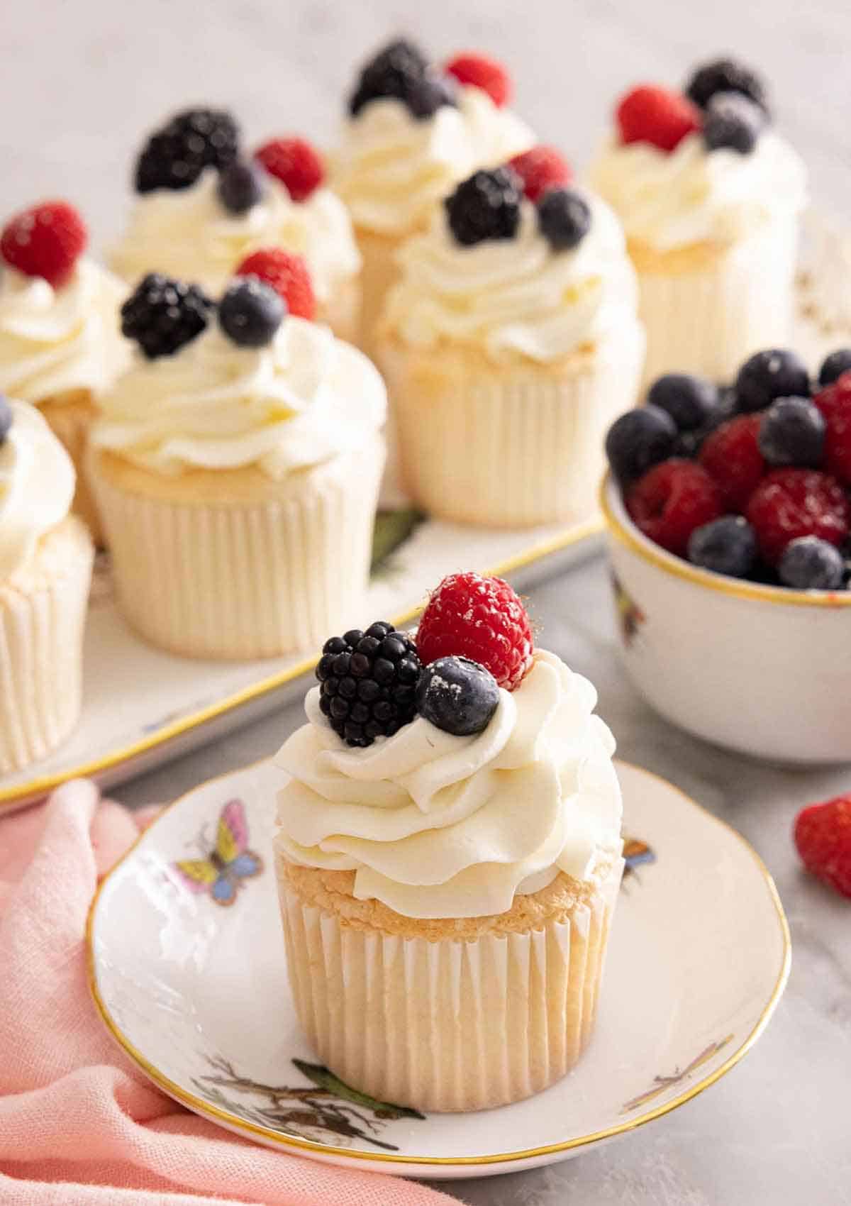 An angel food cupcake on a plate in front of a platter of cupcakes.