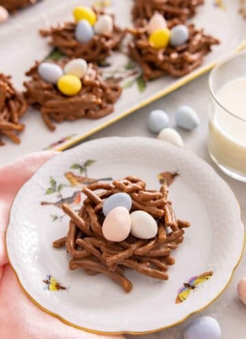 A plate with a birds nest cookie on it by a glass of milk.