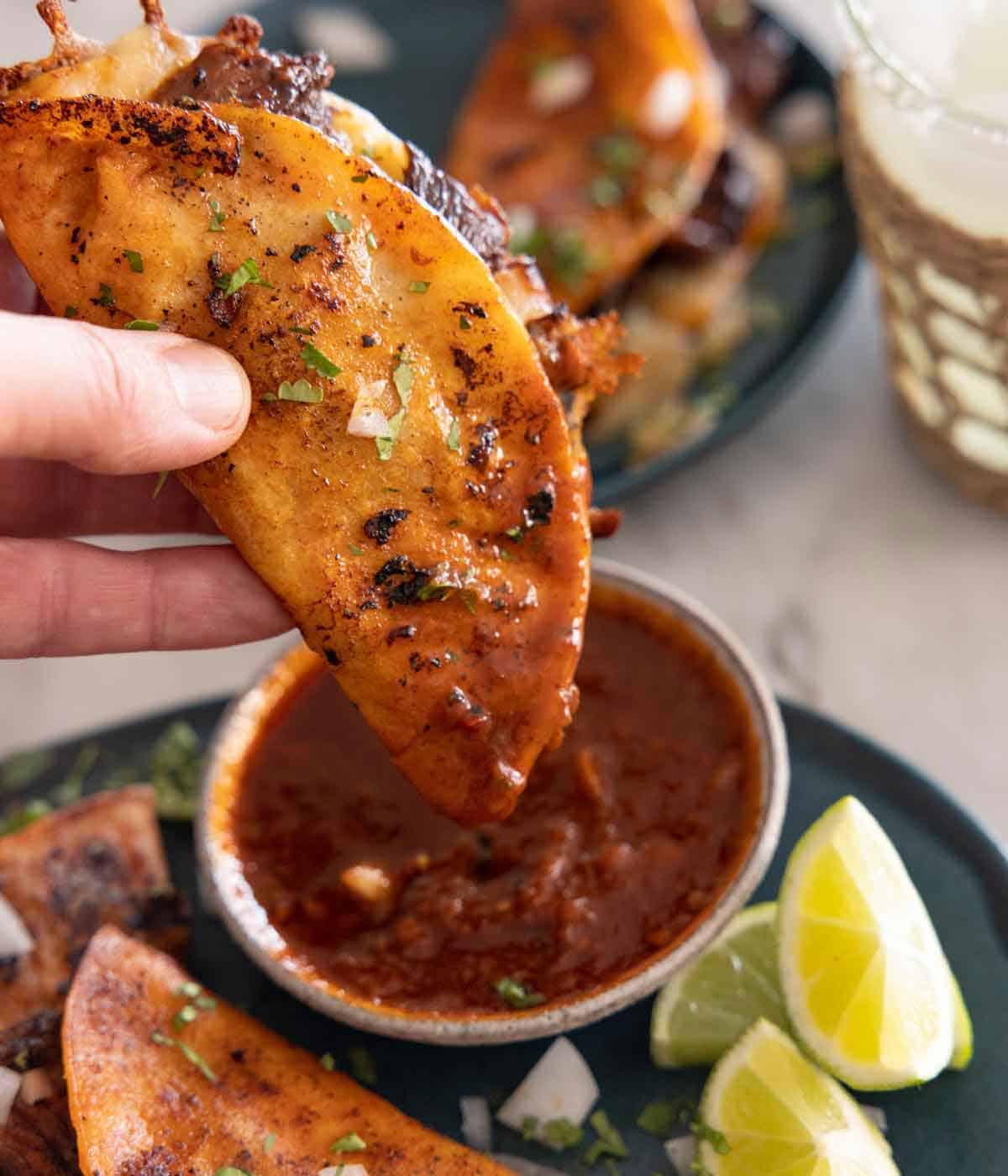 A birria taco dipped in sauce.