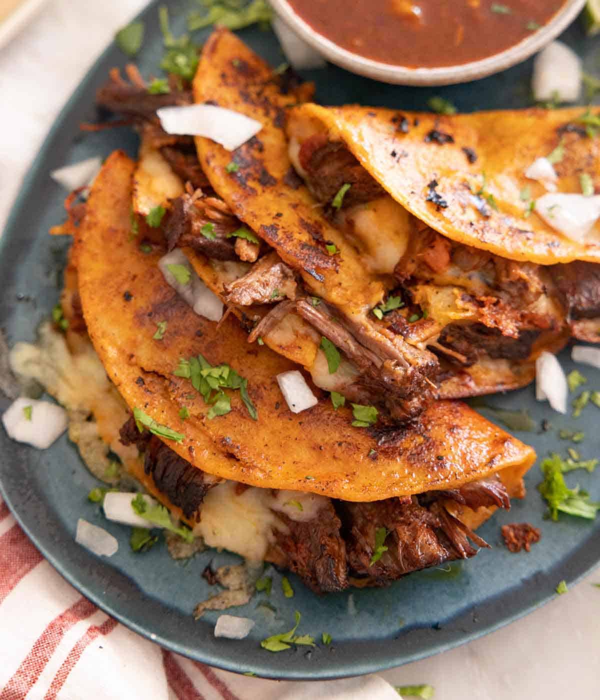 A platter with multiple birria tacos with fresh chopped herbs on top.