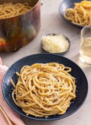 A plate with cacio e pepe with grated cheese and more noodles in the background.