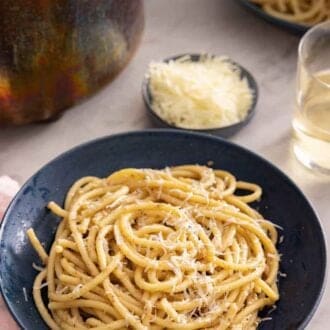 Pinterest graphic of a plate of cacio e pepe by a pinch bowl of grated cheese, a pot, and wine.