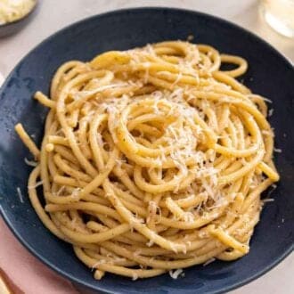 A plate of cacio e pepe by a fork and pink linen.