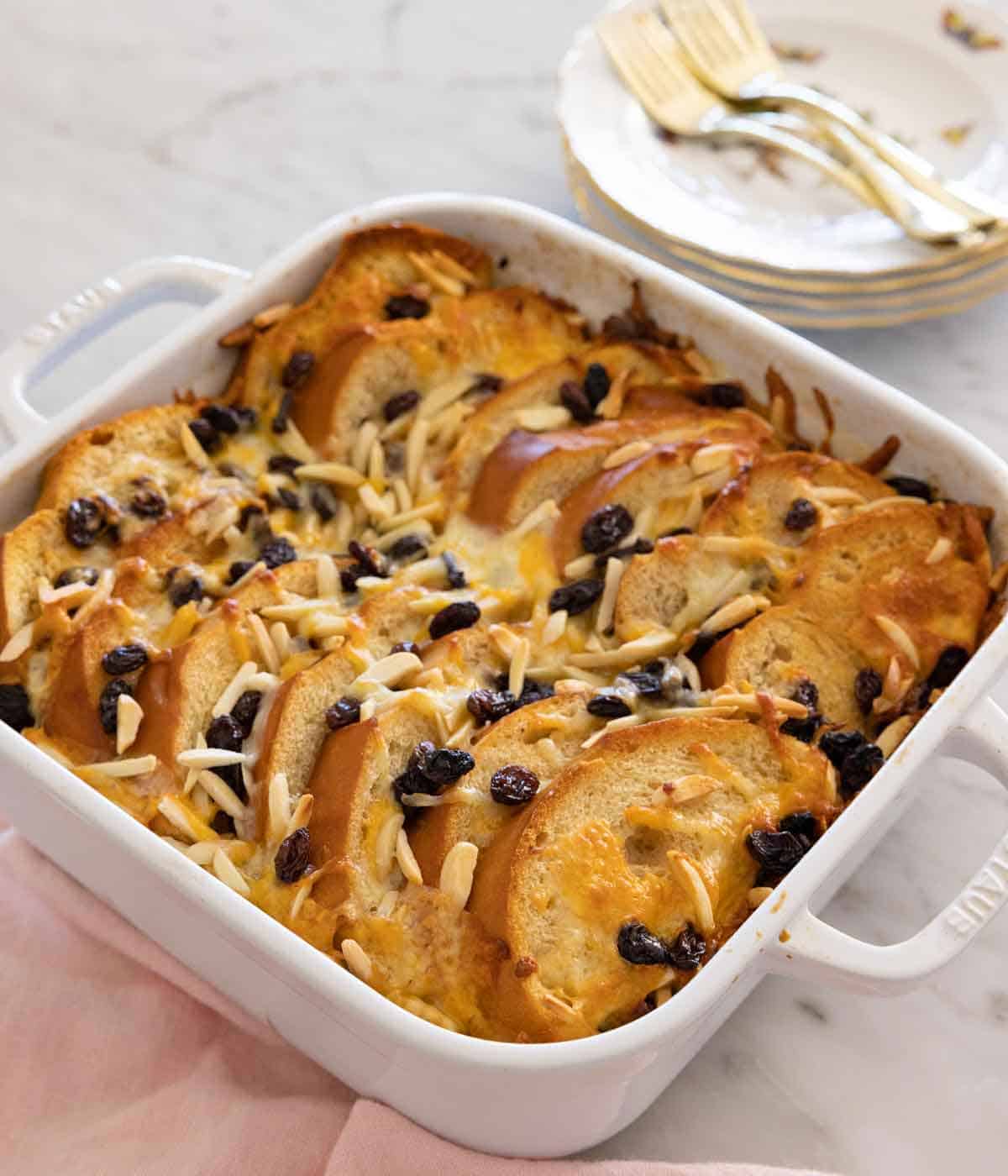 A white baking dish of capirotada with a stack of plates behind it.