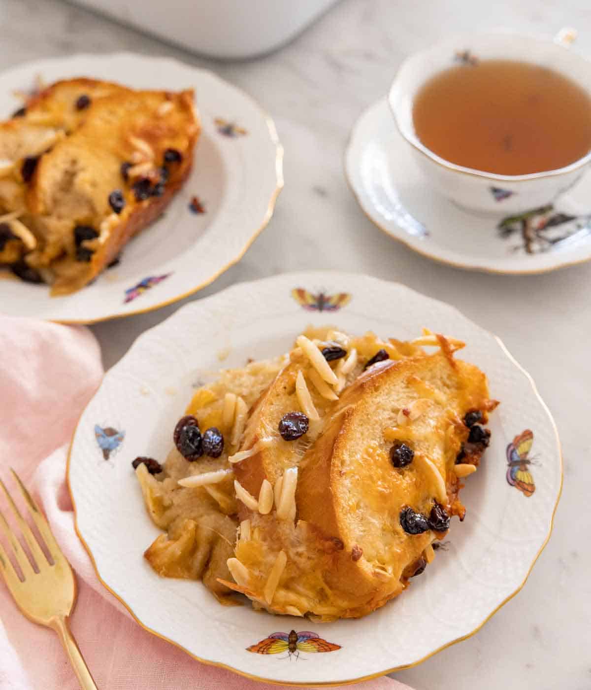 Two plates of capirotada with one in front by a cup of tea.