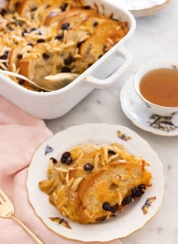 A plate with a serving of capirotada in front of a cup of tea and a baking dish.